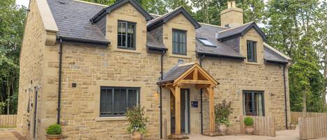 A stone house with a gabled roof, a wooden porch, and a gravel driveway.