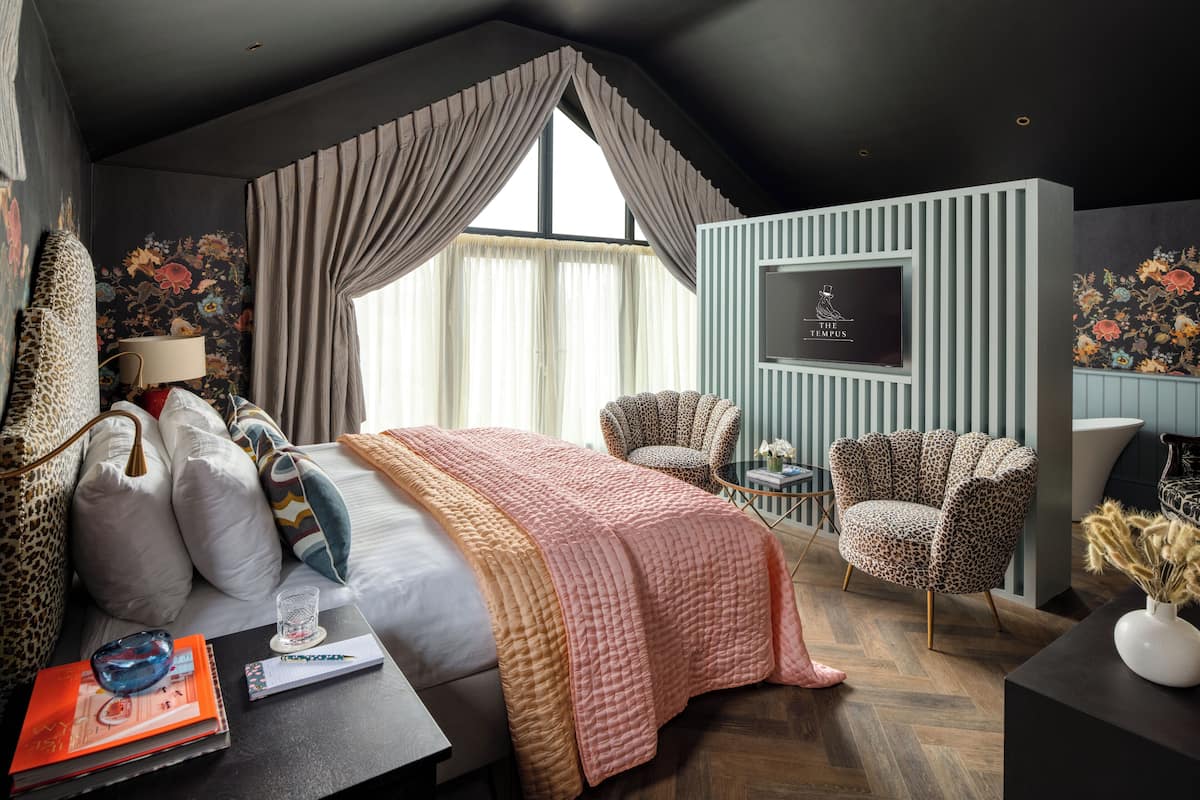 Una habitación de hotel con una cama grande, dos sillones de estampado de leopardo, un televisor y un escritorio con una lámpara y libros.