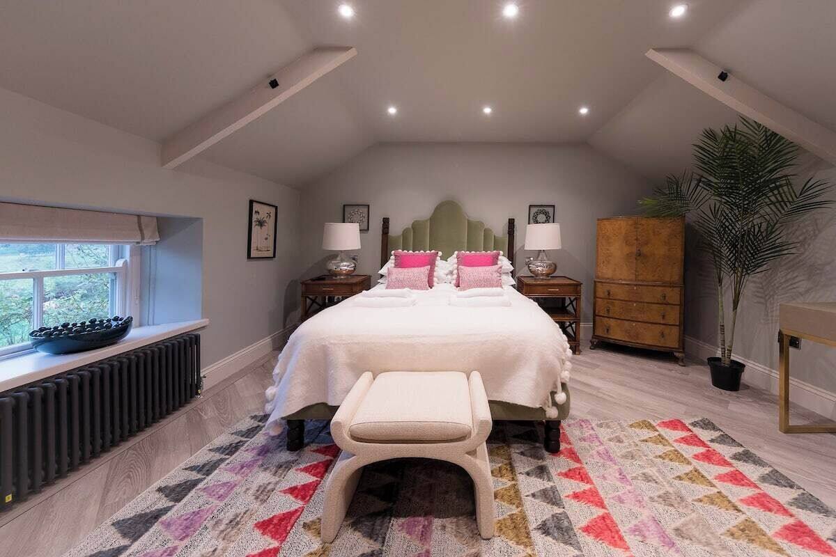 Un dormitorio con cama, mesitas de noche, un radiador, una ventana, una planta y un armario de madera.