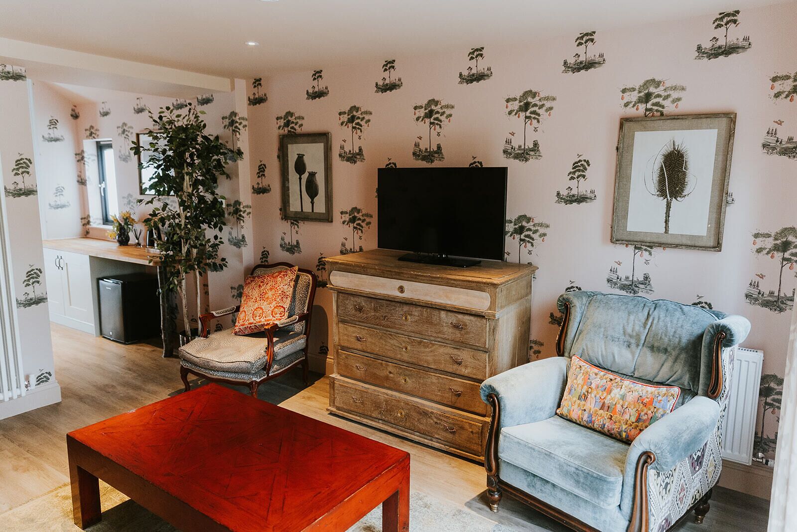 Una sala de estar con una mesa de centro de madera, dos sillones, un televisor sobre un mueble de madera y una planta grande.