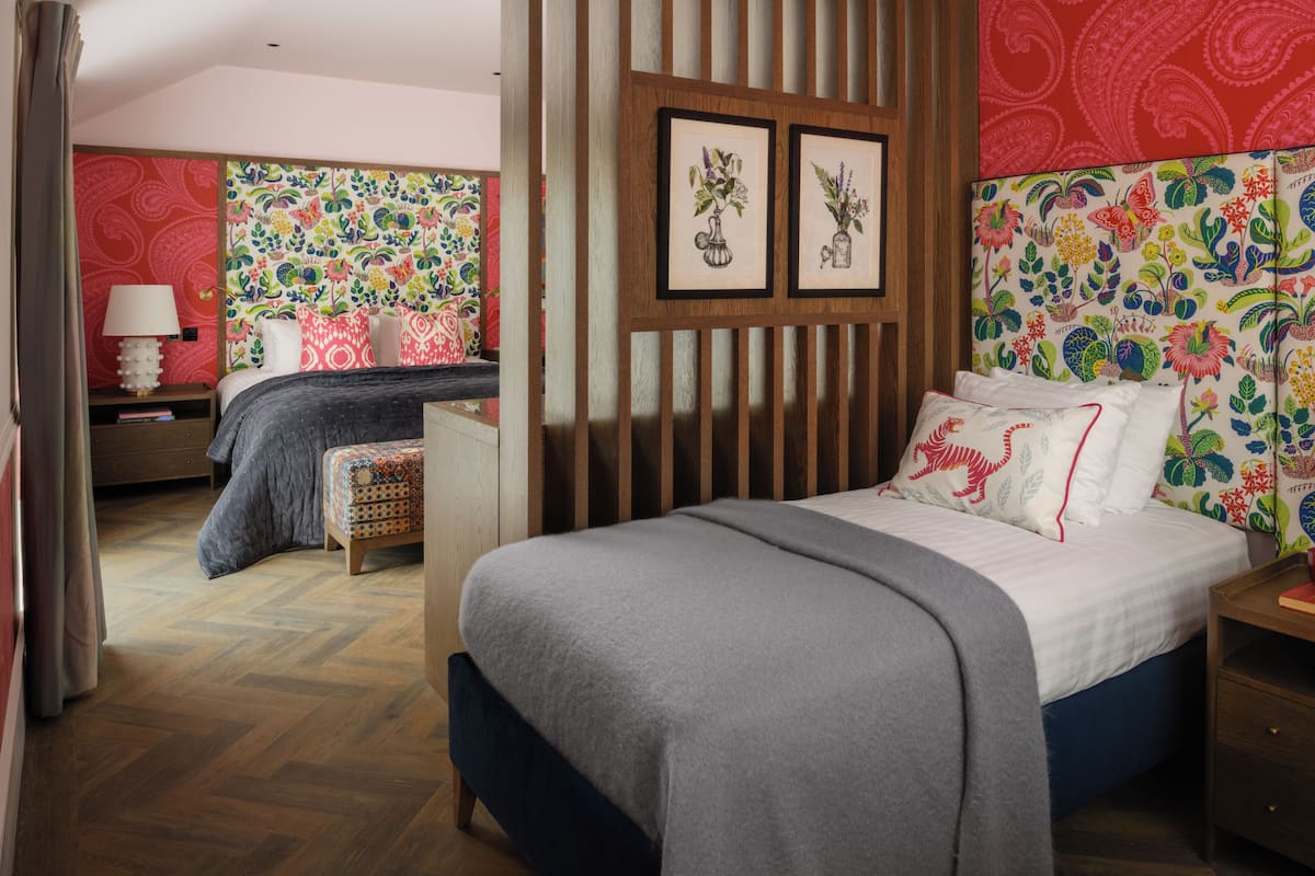 Un dormitorio con cama, mesita de noche, silla y un separador de madera. En la pared hay dos cuadros enmarcados.