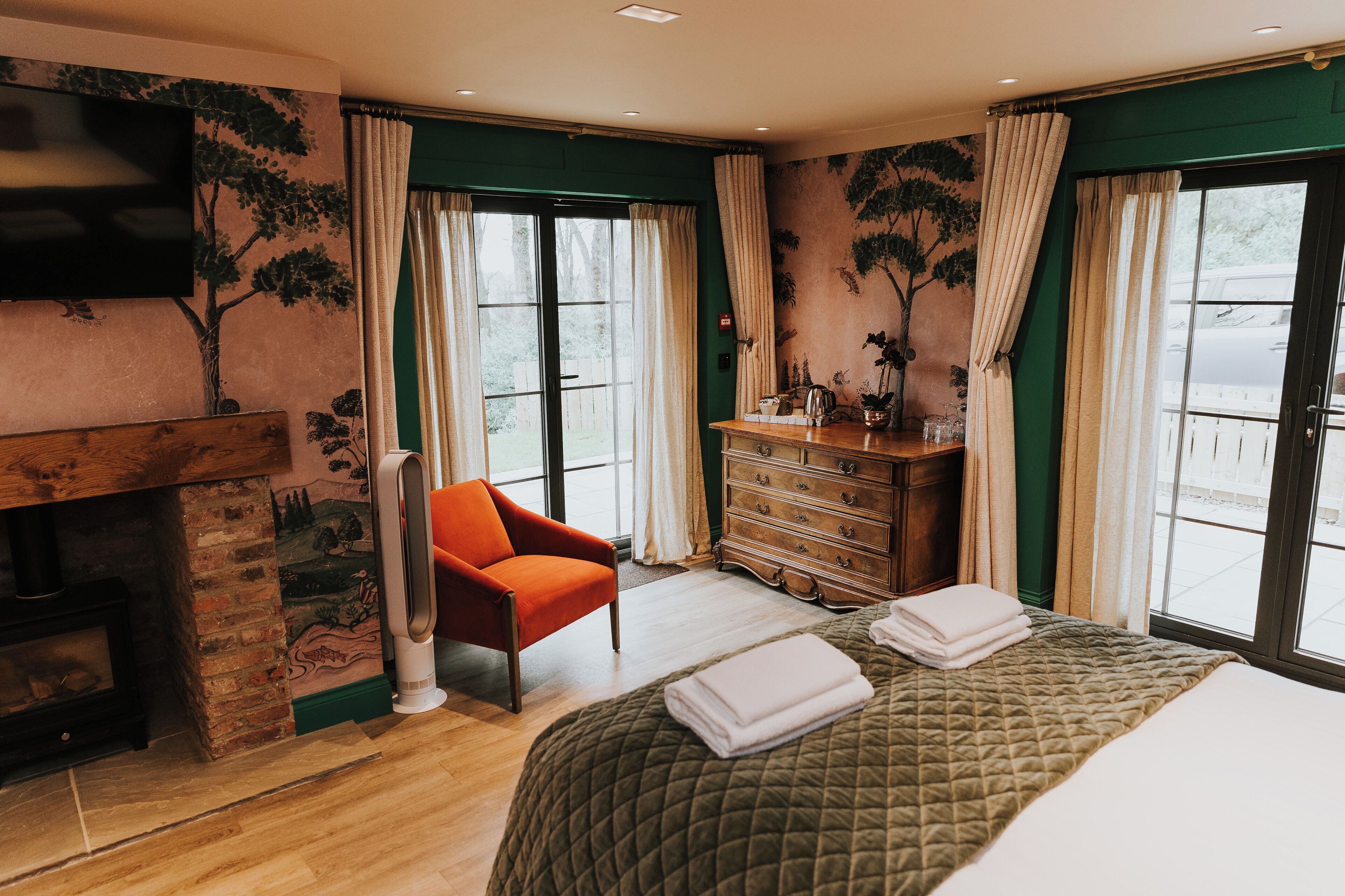 A bedroom with a fireplace, a bed with a quilted bedspread, a wooden dresser, and a chair.