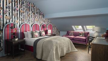 A bedroom with a large bed, a sofa, a desk, and a wall with a striped pattern.