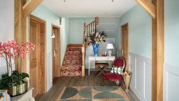 Un couloir avec un escalier en bois, un bureau avec une lampe, une chaise et un vase décoratif.
