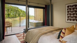 Une chambre avec un grand lit, une vue sur un lac, un balcon avec un fauteuil et une baignoire.