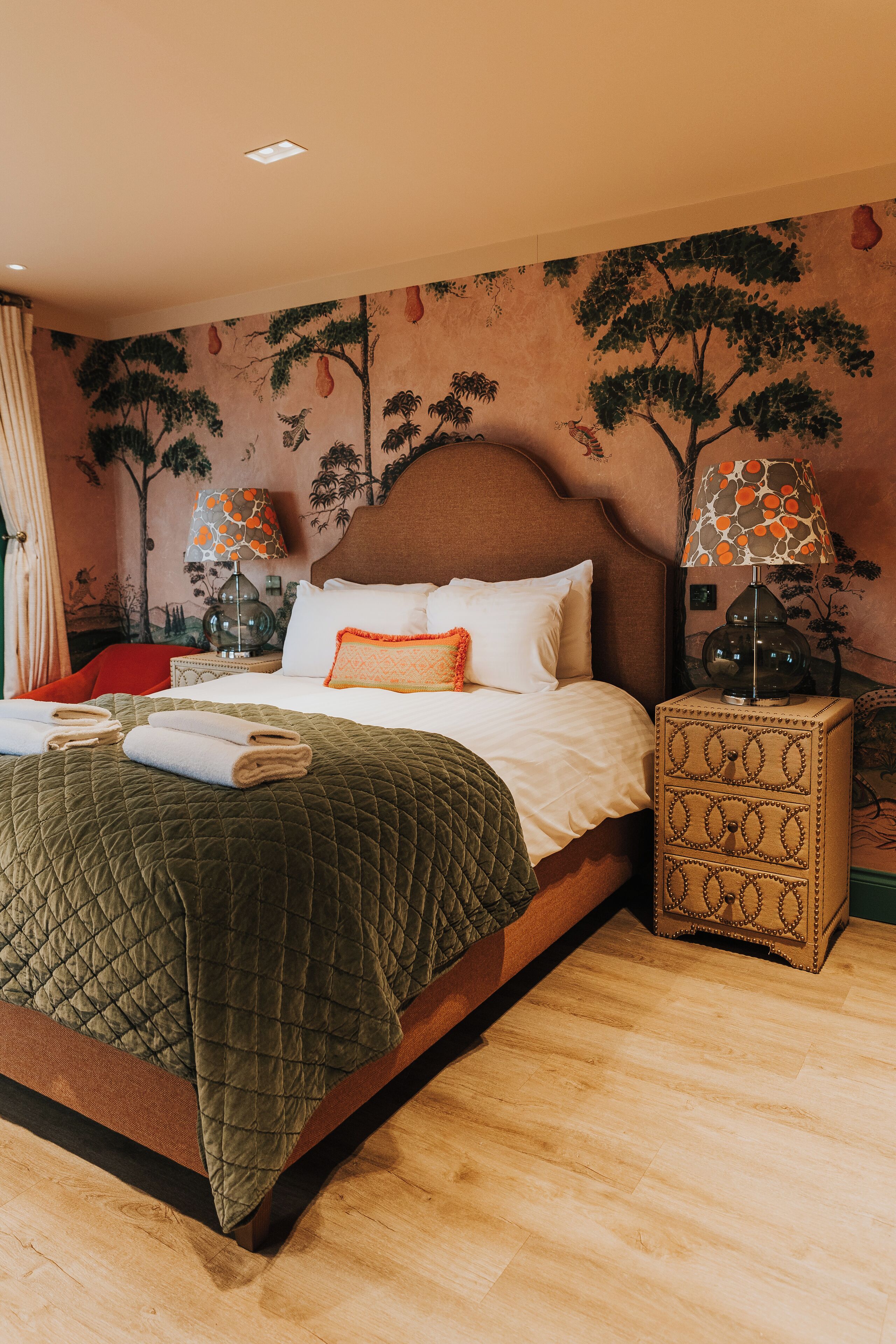 A neatly made bed with a quilted green blanket, a wooden headboard, and a nightstand with a patterned lamp.