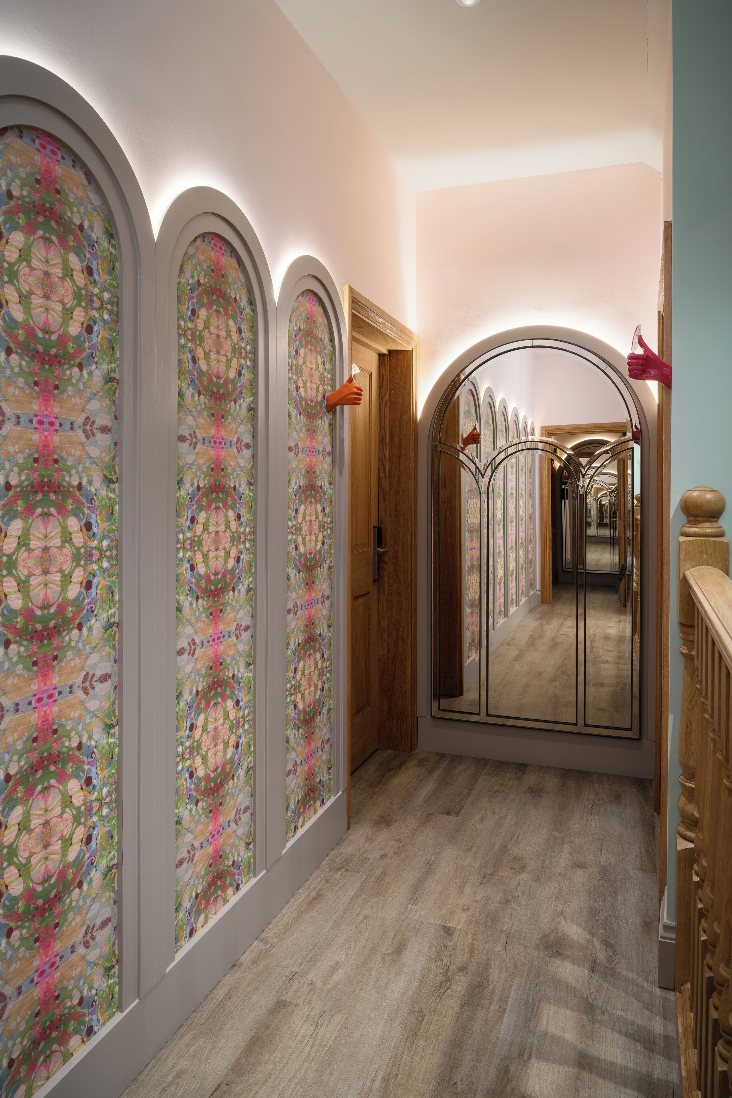 A hallway with a wooden floor, a large mirror, and decorative glass panels.