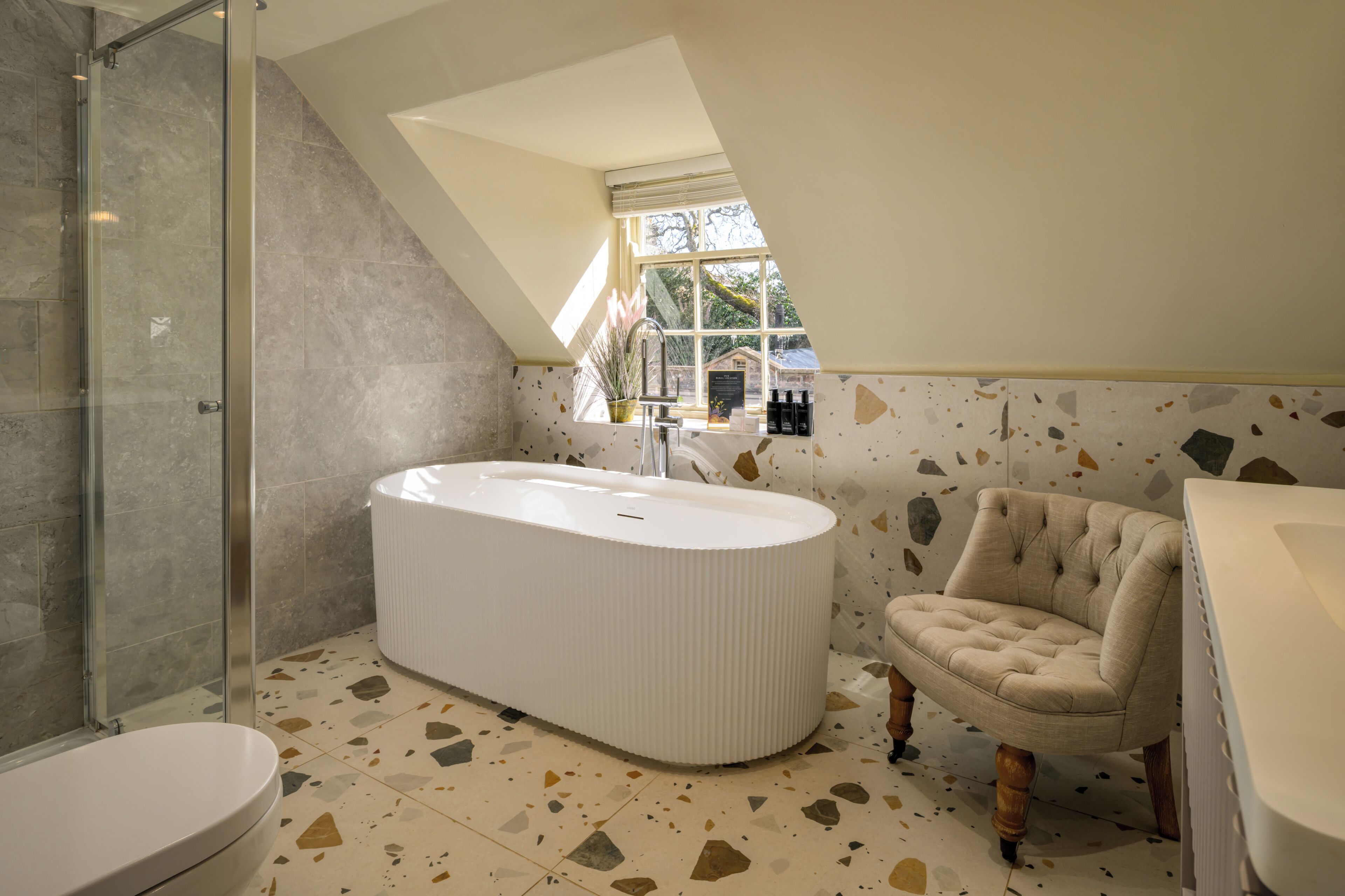 Un baño moderno con una bañera independiente, cabina de ducha con mampara de vidrio y ventana que proporciona luz natural.