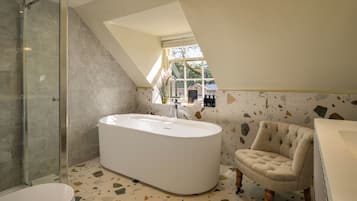 Un baño moderno con una bañera independiente, cabina de ducha con mampara de vidrio y ventana que proporciona luz natural.