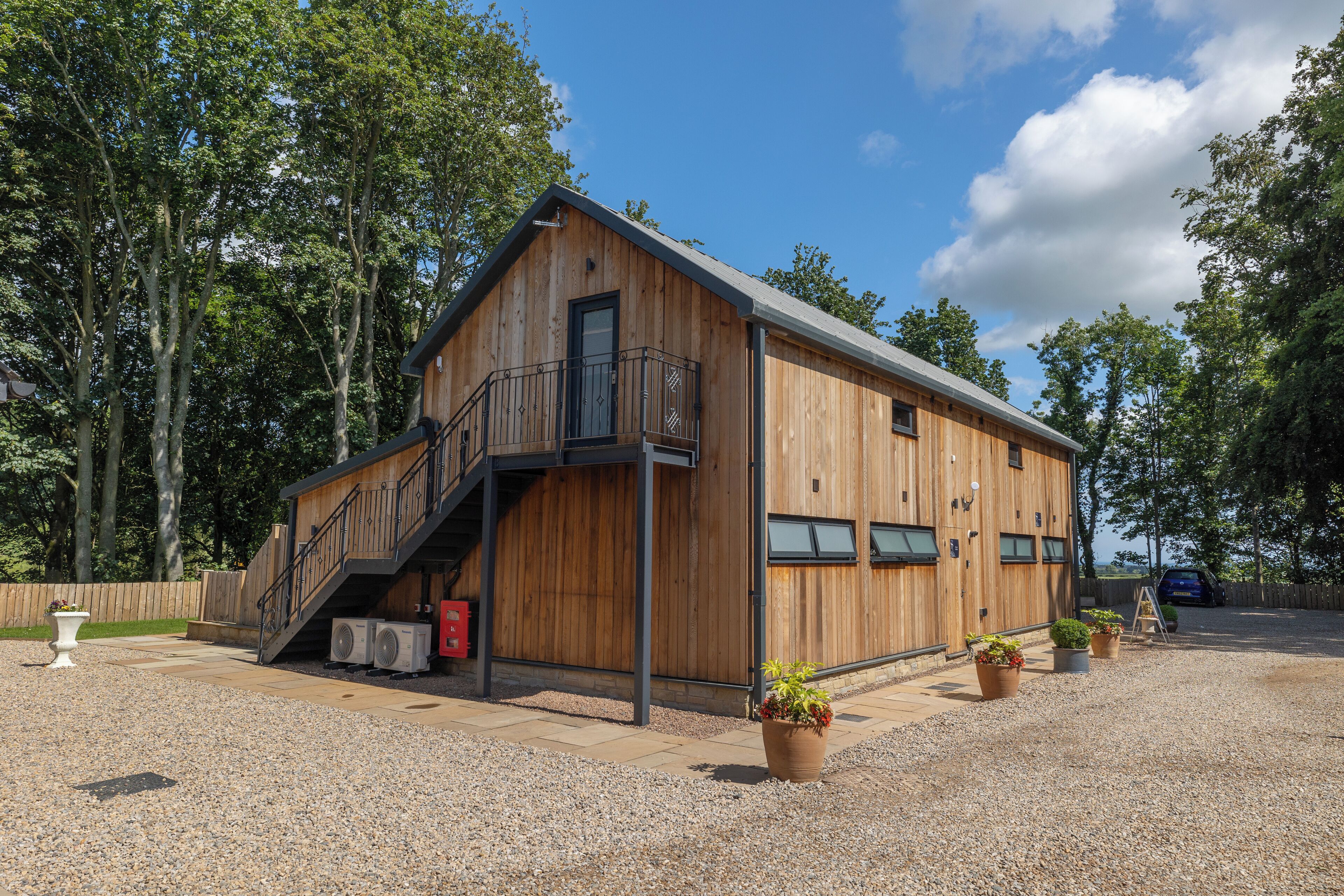 Ein Holzhaus mit Balkon, Treppe und einer Zuwegung mit Kies.
