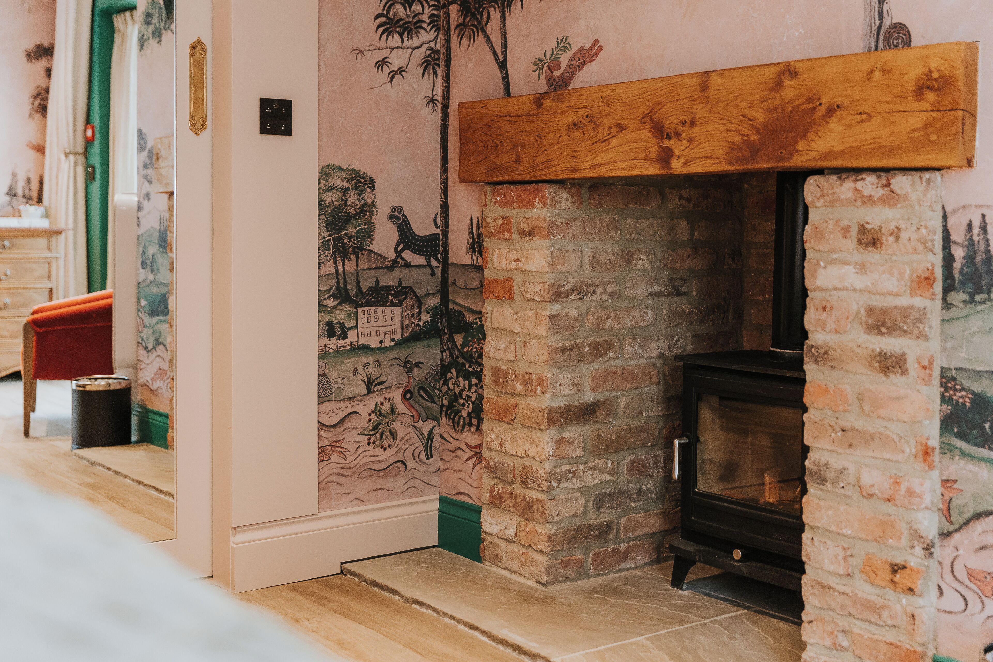 A room with a brick fireplace, a wooden mantel, and a mural on the wall.