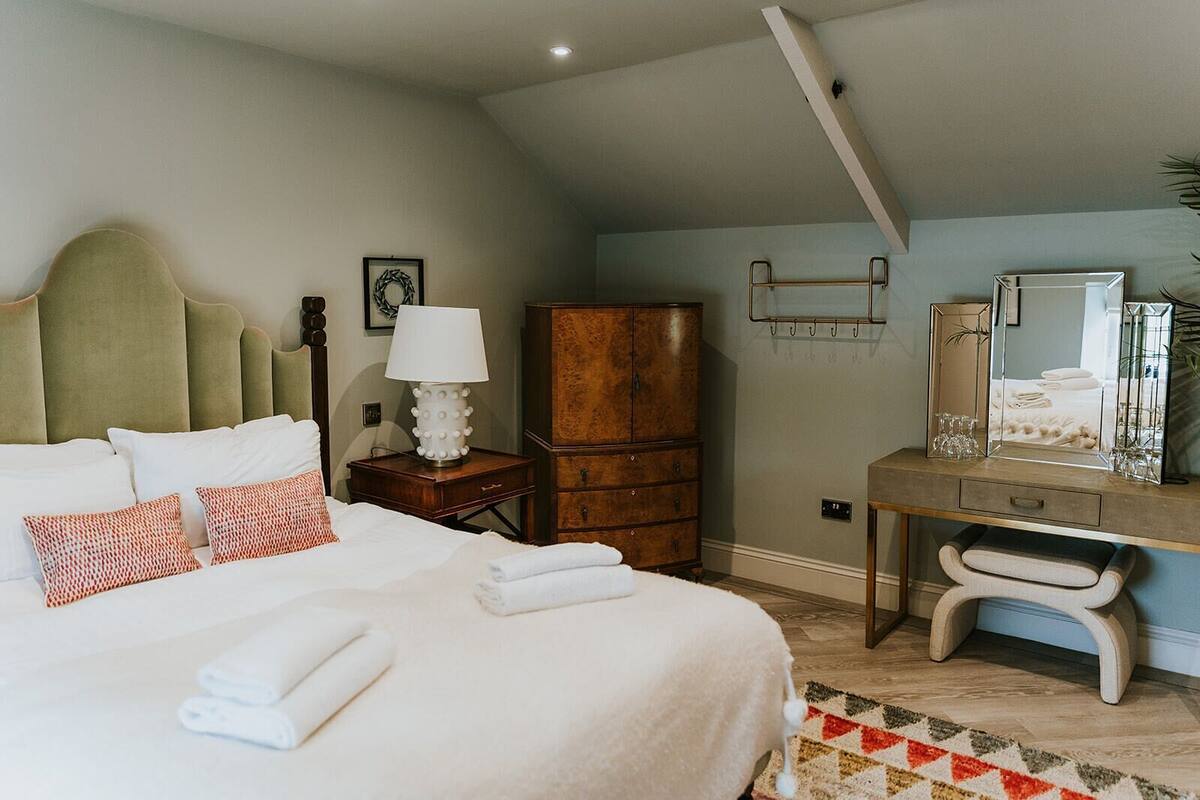 Un dormitorio con cama, mesita de noche, lámpara, cómoda, espejo y un pequeño escritorio con silla.