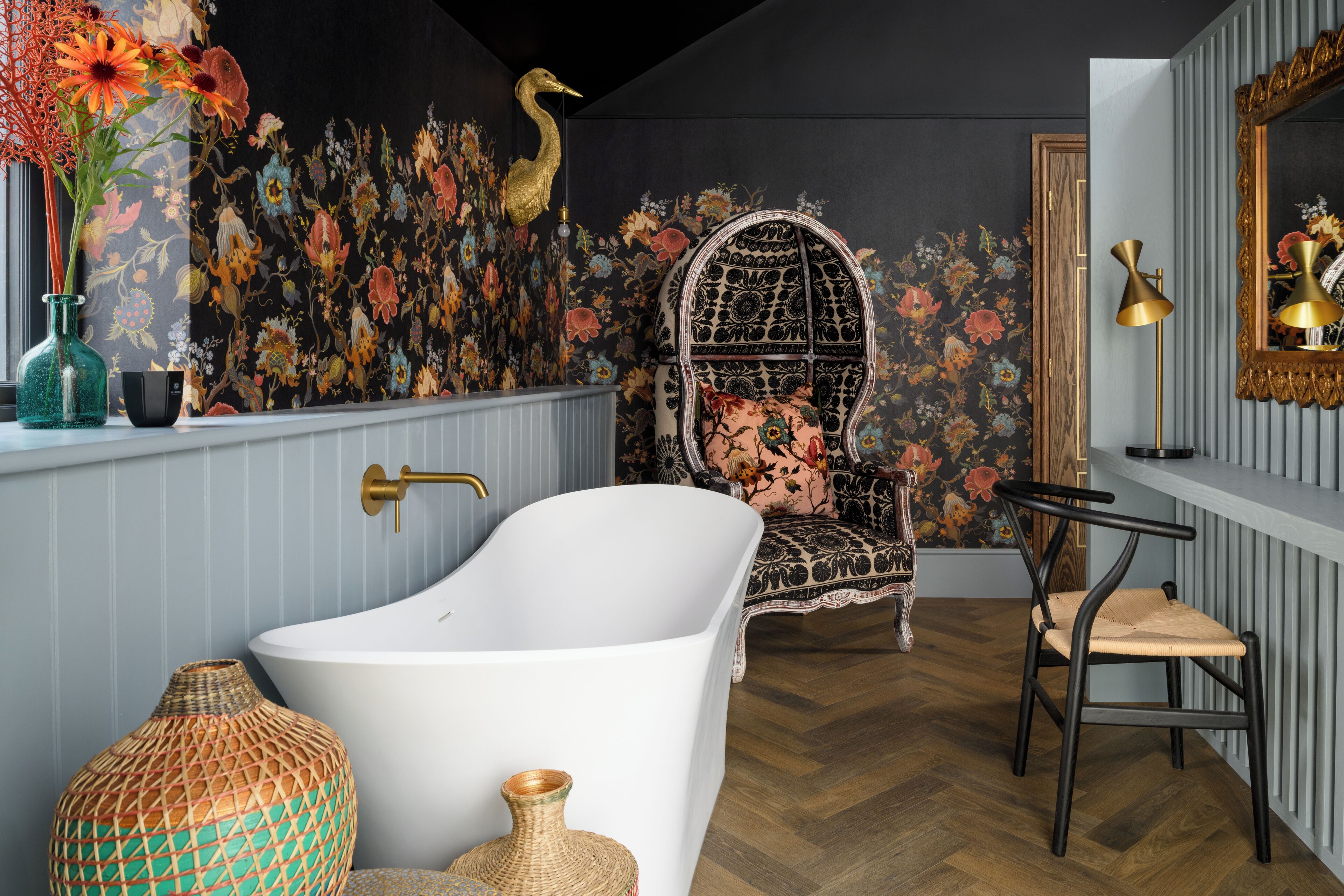 A bathroom with a freestanding bathtub, a decorative chair, and a mirror with a gold frame.