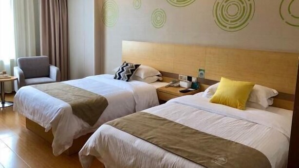 A hotel room with two beds, a chair, a nightstand, and a wall with circular patterns. - Greentree Inn Nantong Qidong Binhai Industrial Park Zone Nanhai Road Express Hotel (Nantong)