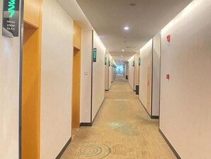 Un pasillo de hotel con puertas numeradas, una alfombra con diseños circulares e iluminación empotrada en el techo.