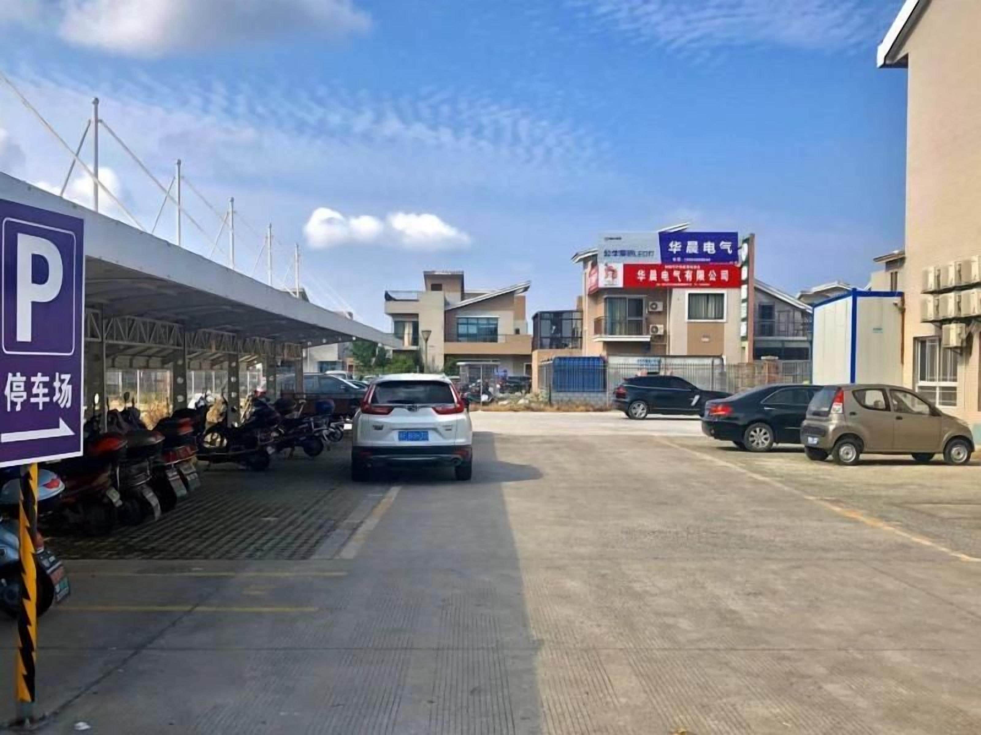 A parking lot with a covered waiting area, a building with signage, and parked cars.