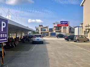 Un estacionamiento con zona de espera cubierta, un edificio con señalización y automóviles estacionados.