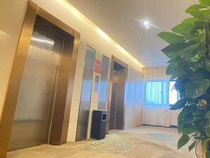 Et hotellobby med elevatorer, en skraldespand og en potteplante.