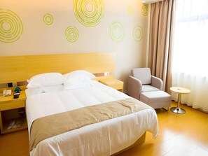 Quarto de hotel com cama, uma cadeira, uma mesa pequena e mesa de cabeceira com telefone e controle remoto.
