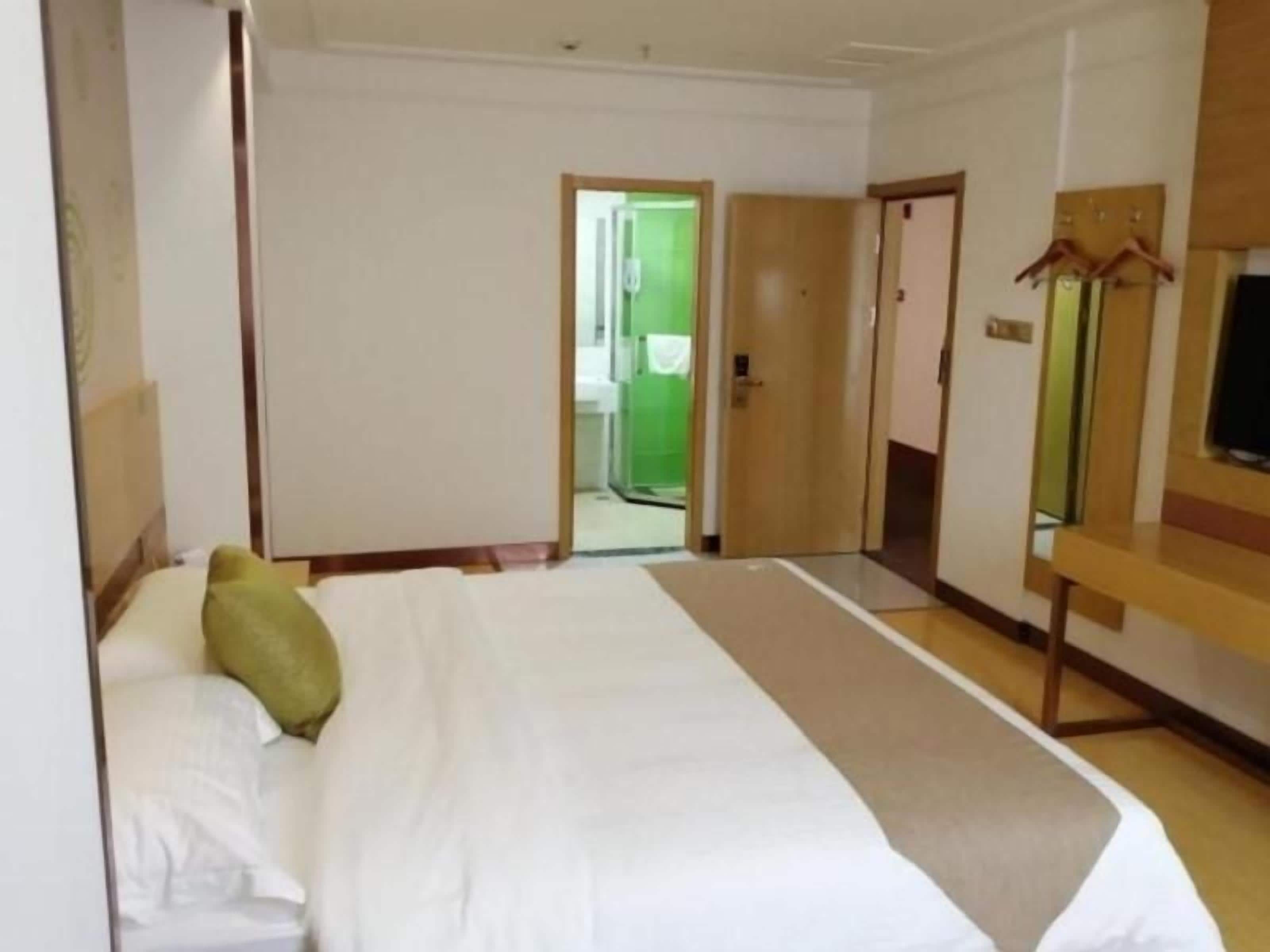 A hotel room with a large bed, a television on the wall, and a door leading to a hallway.