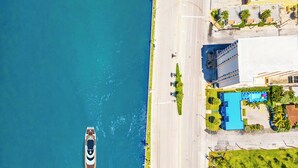 An aerial view of a coastal property with a swimming pool, a boat dock, and a road adjacent to the beach.