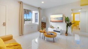 A modern living room with a sofa, two round coffee tables, a TV, and a large window with curtains.