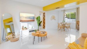 A modern living room with a large mirror, a painting, a dining area with wooden chairs, and a yellow accent wall.