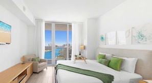 Una habitación de hotel moderna con una cama grande, un escritorio, una silla y vistas a la ciudad y al agua a través de amplios ventanales.