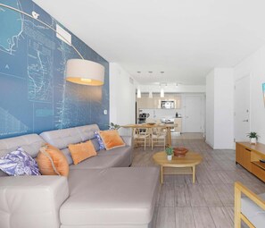 A modern living room with a sofa, coffee table, and a kitchen in the background.