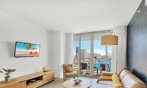 Ein modernes Wohnzimmer mit großem Fenster, einem Flachbildfernseher, einer Couch, einem Couchtisch und einer Pflanze.