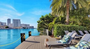 A poolside area with lounge chairs, a table with drinks, and a view of the city skyline. - Apartment w/ Balcony +  Amazing Pool (Hallandale Beach)