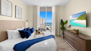 Een hotelkamer met een bed, een televisie, een plant en uitzicht op de oceaan.