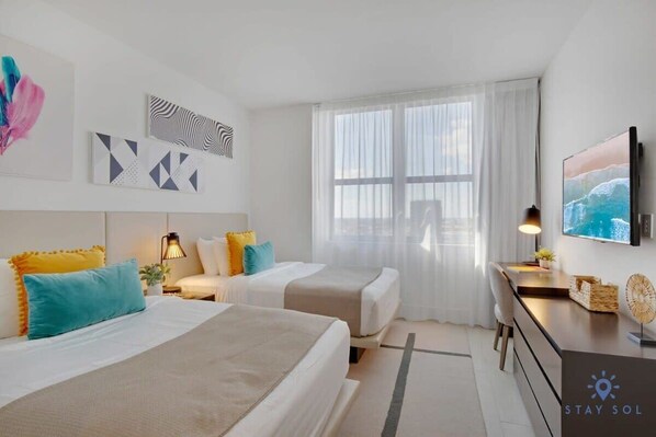 A modern hotel room with two beds, a desk, and a TV.