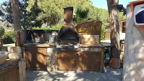 An outdoor stone fireplace with a chimney, surrounded by stone walls and wooden furniture. - Villa in Chia 5 minutes from the most beautiful beaches (Chia)