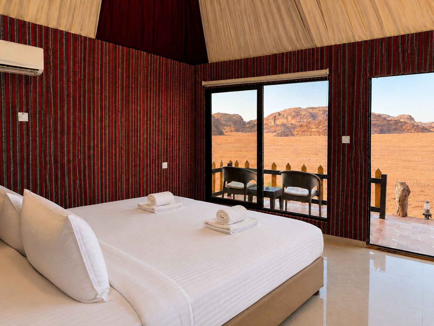 Habitación de hotel con una cama grande, vista al desierto y un balcón con sillas.