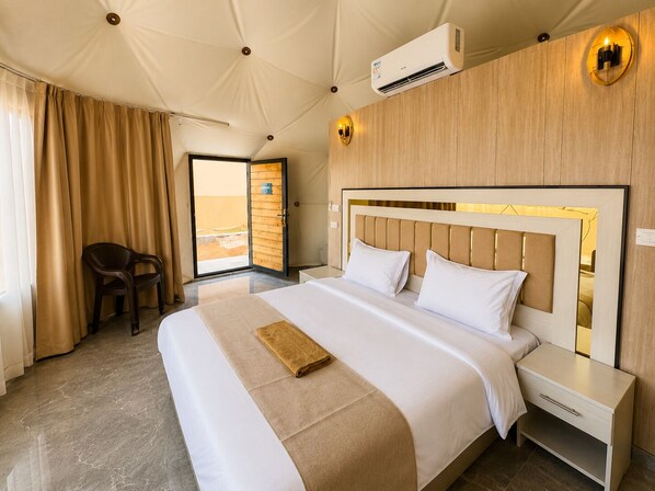 Una habitación de hotel con una cama grande, cabecera de madera, mesita de noche, una silla y un equipo de aire acondicionado.