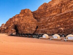 A desert landscape with rock formations and a row of tents. - Shaheen Camp wadi rum (Wadi Rum)