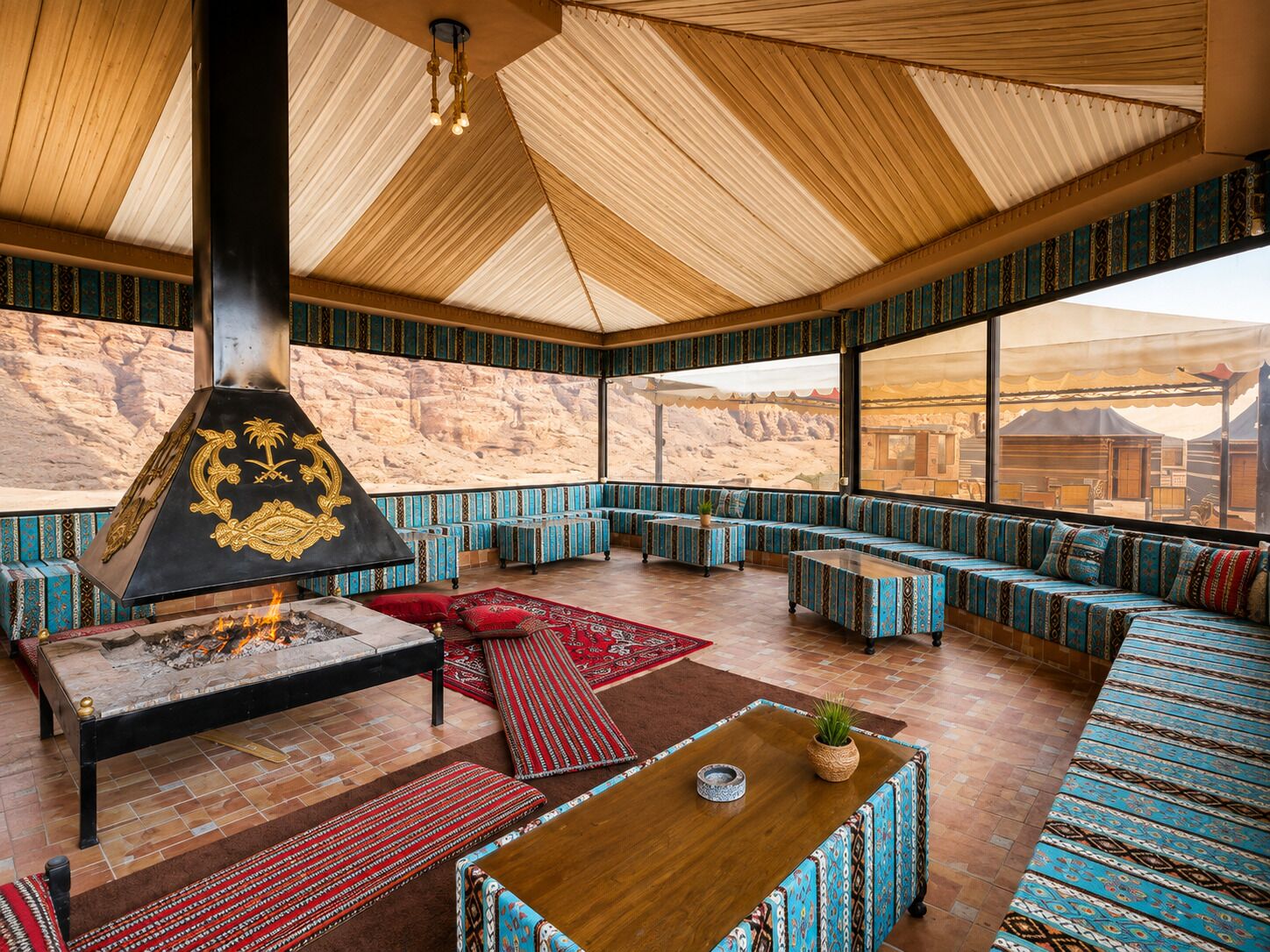 A spacious room with a high ceiling, a large fireplace, and a view of the desert through large windows.