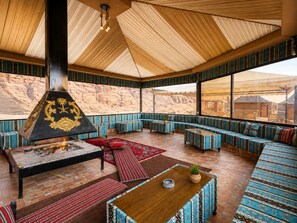 A spacious room with a high ceiling, a large fireplace, and a view of the desert through large windows. - Shaheen Camp wadi rum (Wadi Rum)