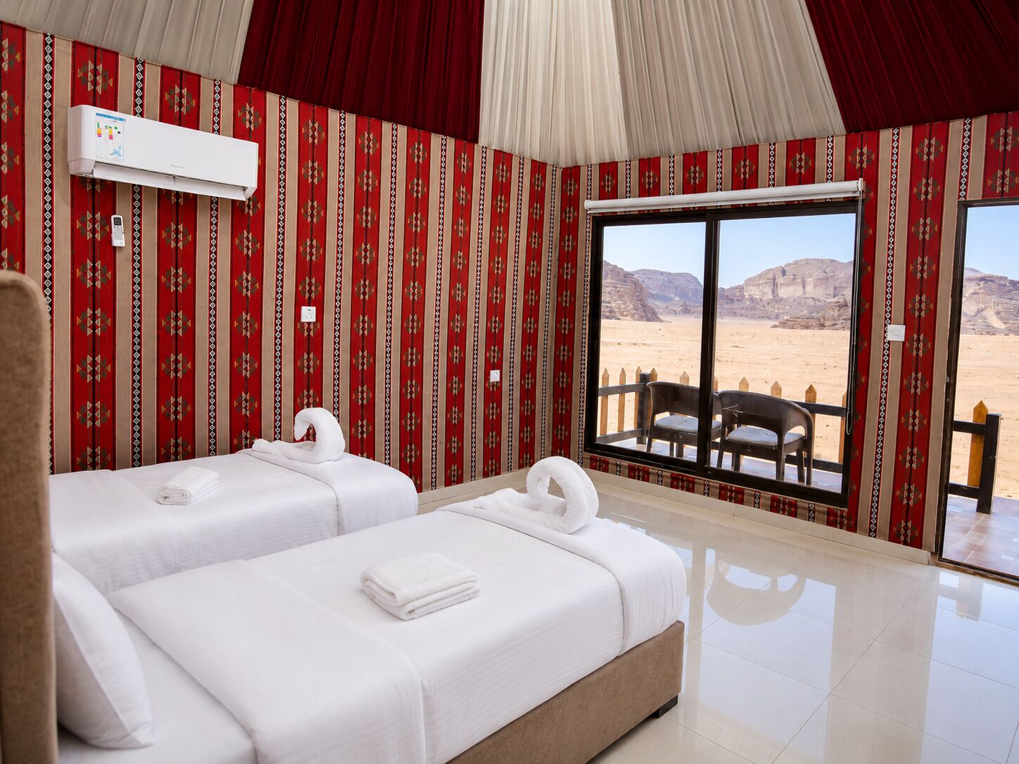 Habitación de hotel con dos camas, un ventanal con vista al desierto y una pared con diseño rojo.