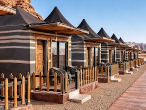 A row of chalet-style accommodations with wooden facades and black roofs, set against a mountainous backdrop.