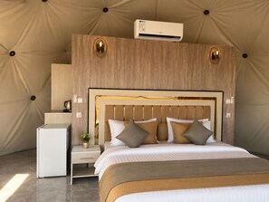 A bedroom with a large bed, a bedside table, a nightstand, an air conditioning unit, and a wall-mounted lamp. - Shaheen Camp wadi rum (Wadi Rum)