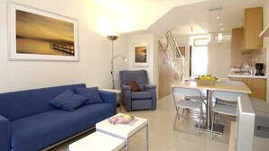 Ein modernes Wohnzimmer mit einem blauen Sofa, einem kleinen weißen Tisch und einem Essbereich mit Stühlen.