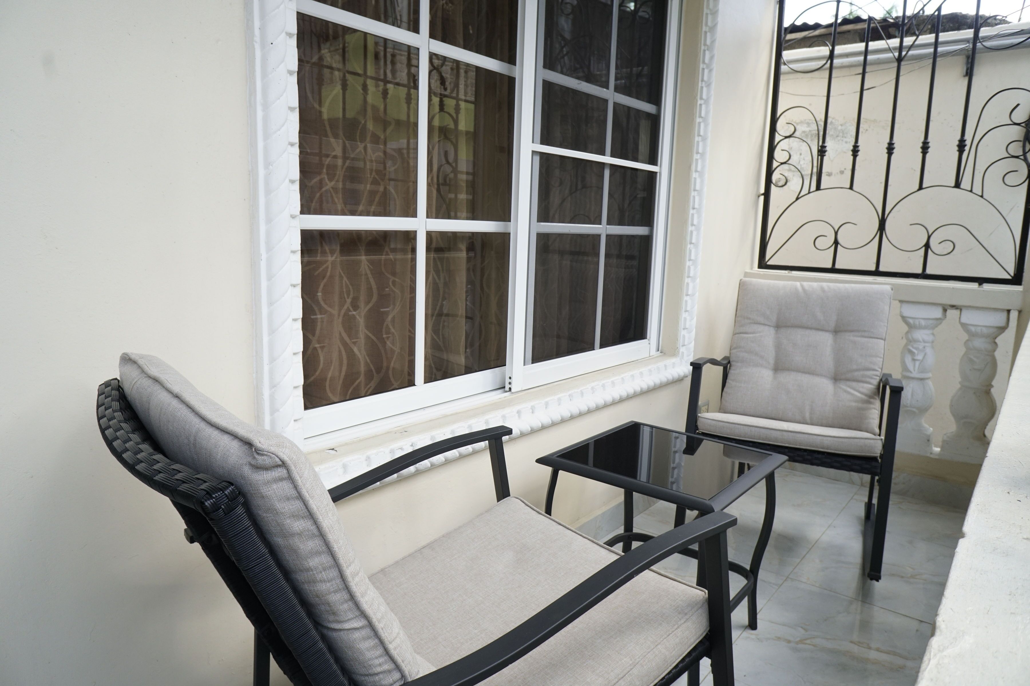 Un balcon avec une chaise blanche dotée d’un coussin, une petite table et une fenêtre ornée de motifs en fer forgé.