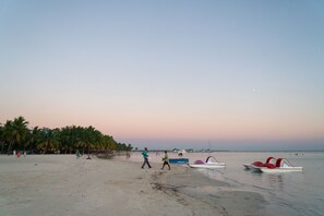 A beach with people walking, palm trees, and boats on the sand. - Villa Gumio - Your Comfort In Boca Chica Beach 2 Bedroom Apts by RedAwning (Boca Chica)