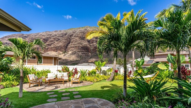 Un patio trasero con un suelo de piedra, mobiliario exterior y una variedad de plantas tropicales.