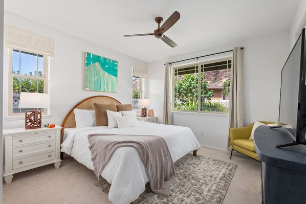 A bedroom with a bed, nightstands, a television, and large windows.