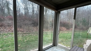 Un patio abrité doté de grandes portes vitrées, d’un banc en bois et offrant une vue sur une cour verdoyante avec des arbres.