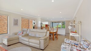 Ein geräumiges Wohnzimmer mit einem beigefarbenen Sofa, einem Essbereich mit Holzsesseln und einer durchgehenden Tür sichtbaren Küche.