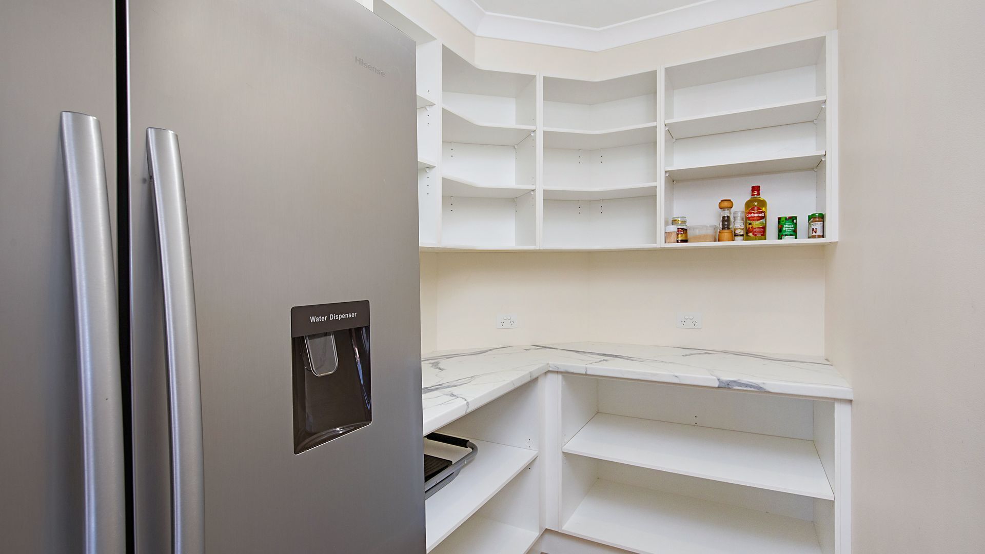 Une cuisine équipée d’un distributeur d’eau, de meubles blancs et d’un plan de travail en marbre.